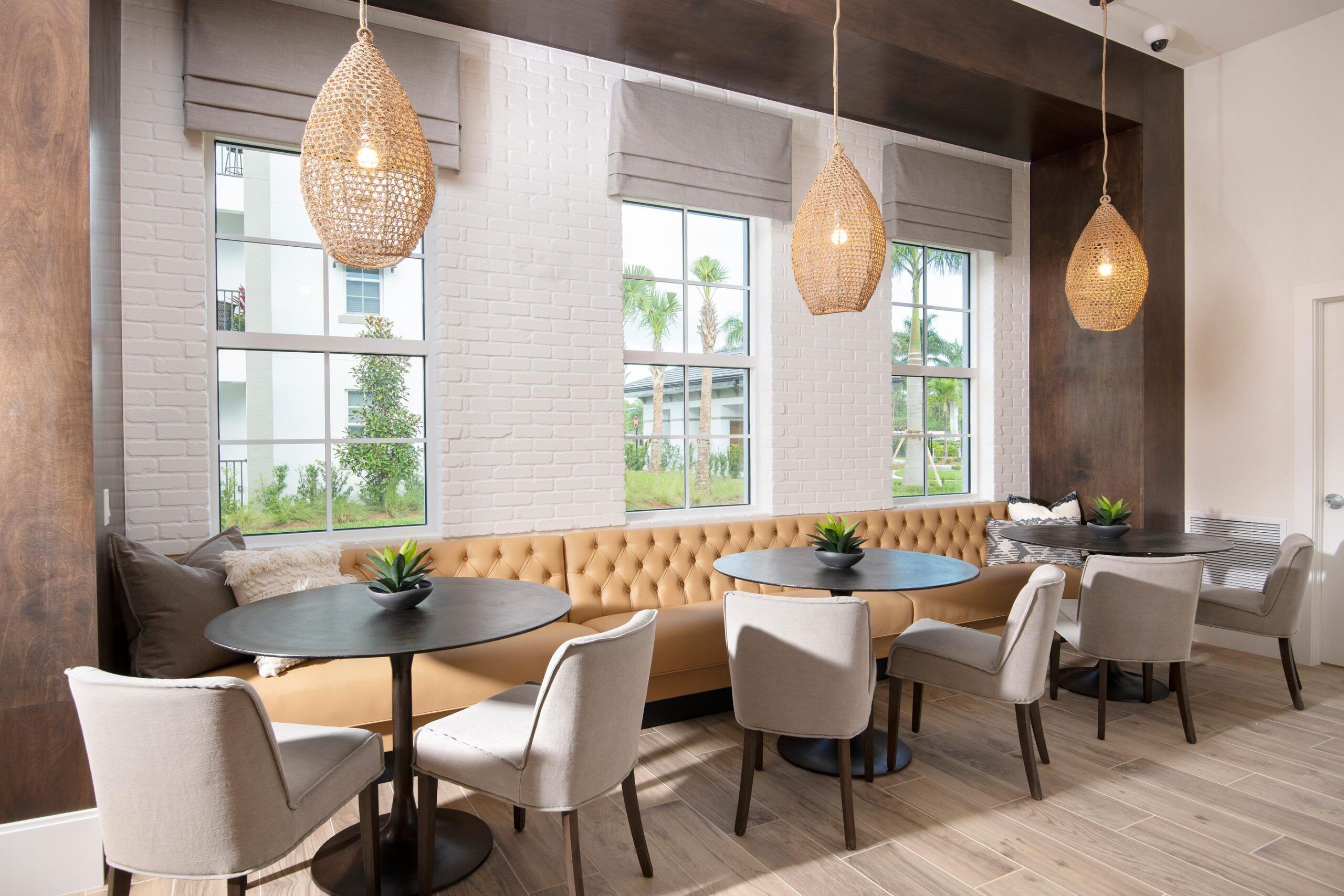 Inspira Naples Modern cafe with tan sofa, round tables, gray chairs, woven lights, and large windows letting in natural light.
